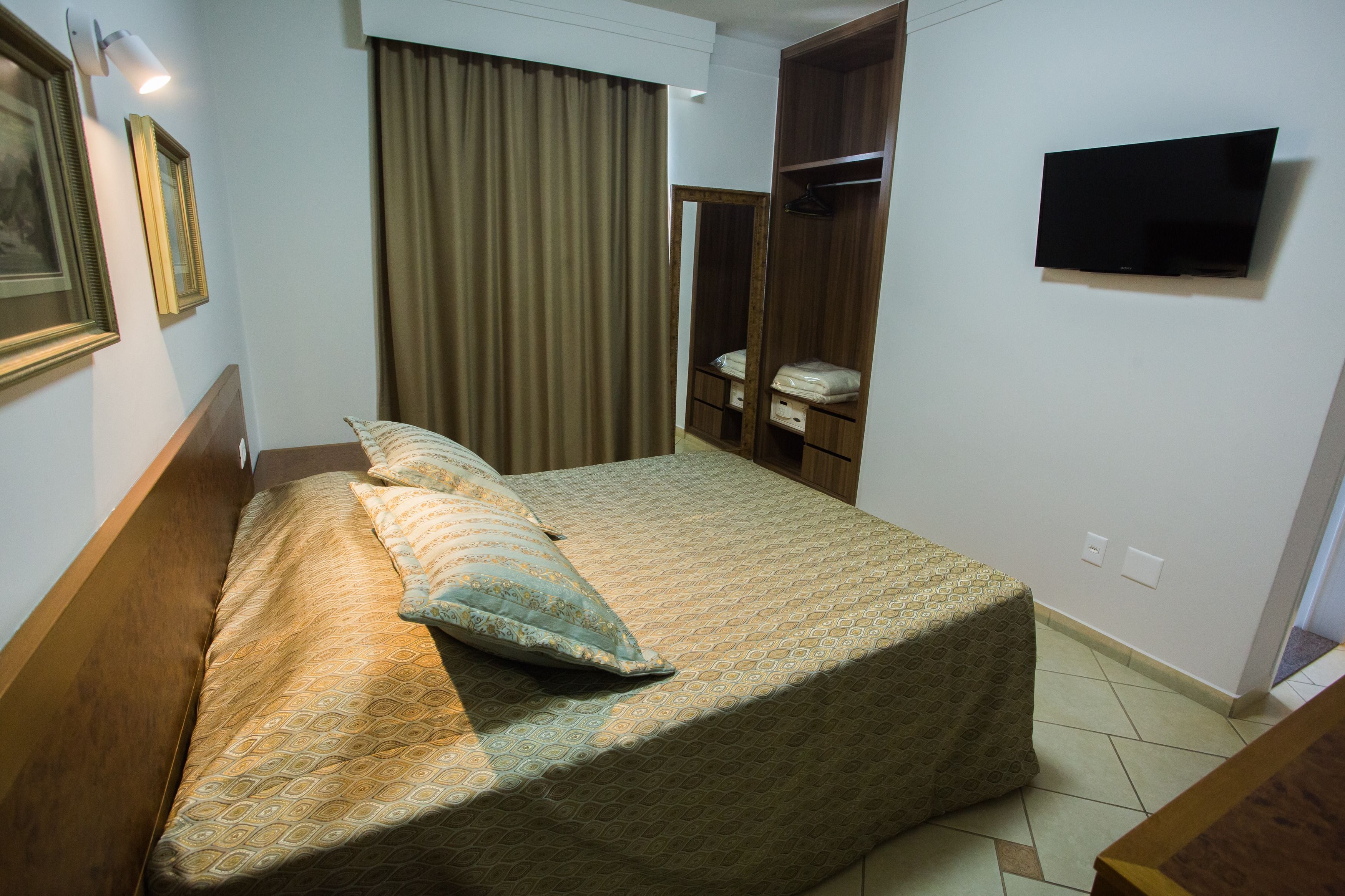 Una habitación de hotel con una cama, un armario, un televisor y un espejo.