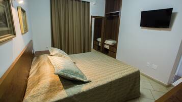 Una habitación de hotel con una cama, un armario, un televisor y un espejo.