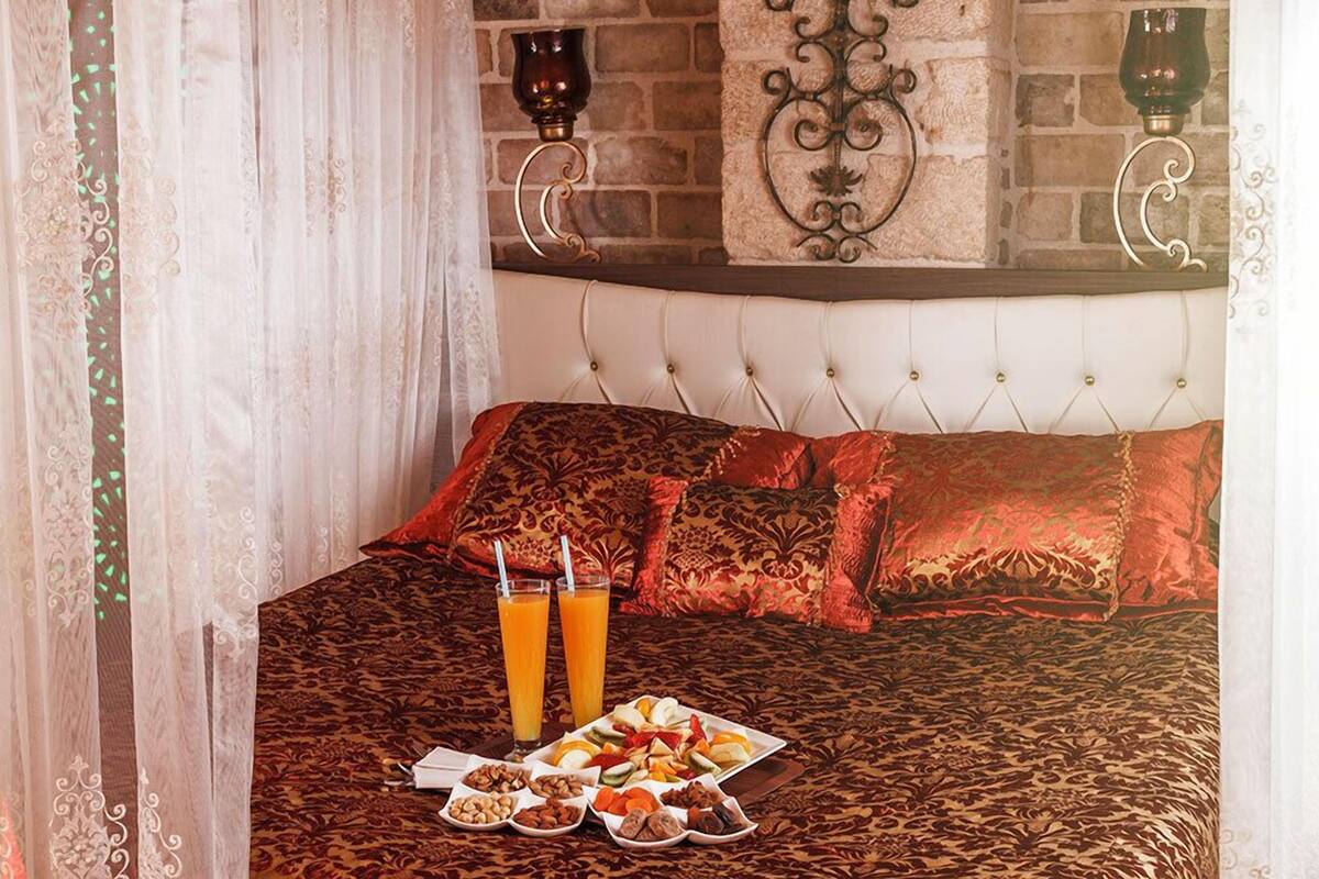 A bed with a patterned bedspread, two pillows, a tray of snacks, and two glasses of orange juice.