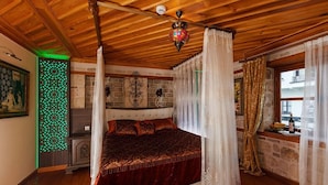 Uma cama com dossel, com edredom vermelho, teto de madeira e parede de pedra.