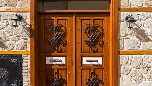 Parede de pedra com uma porta dupla de madeira, detalhes em metal decorativo e duas lanternas fixadas na parede.