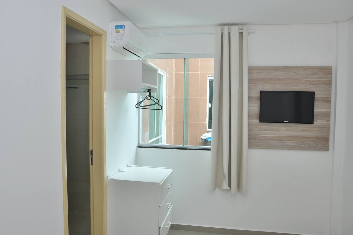 Une chambre d’hôtel moderne dotée d’une grande fenêtre, d’un téléviseur fixé au mur et d’une armoire blanche.