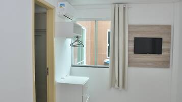 Quarto de hotel moderno com uma janela grande, uma televisão montada e um guarda-roupa branco.