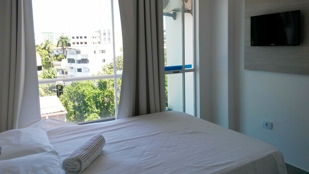 A hotel room with a large bed, a TV mounted on the wall, and a window with curtains. - Hotel Pousada Salvador (Salvador)