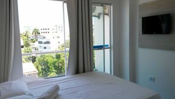 Quarto de hotel com cama grande, televisão presa na parede e janela com cortinas.