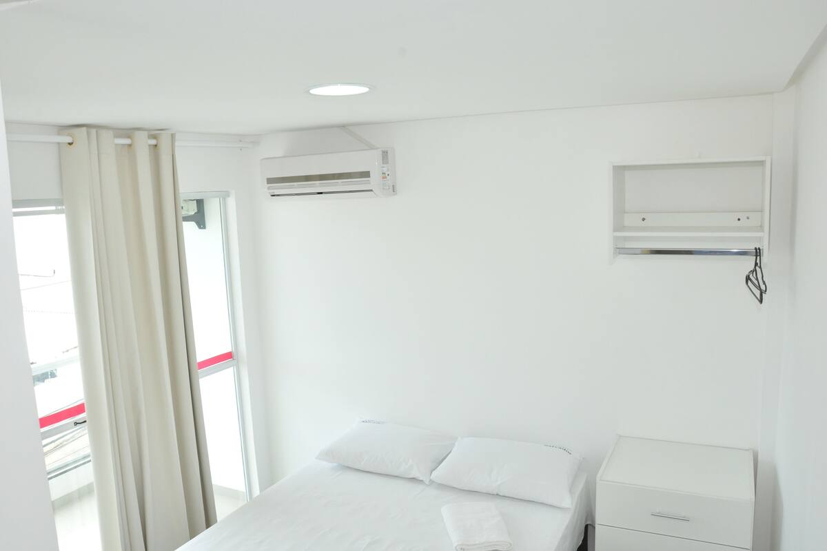 Une chambre d’hôtel avec un lit, une table de chevet, un climatiseur fixé au mur et une fenêtre avec des rideaux.