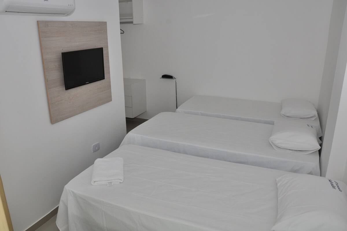 Une chambre d’hôtel avec deux lits simples, un téléviseur à écran plat fixé sur un panneau en bois, une table de chevet et une lampe.