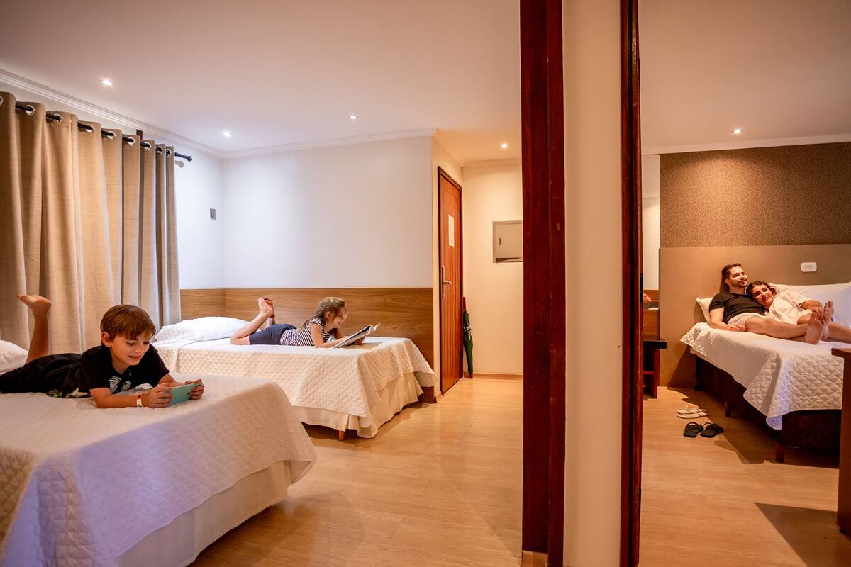 A hotel room with three beds, a wooden floor, and a door leading to another room.