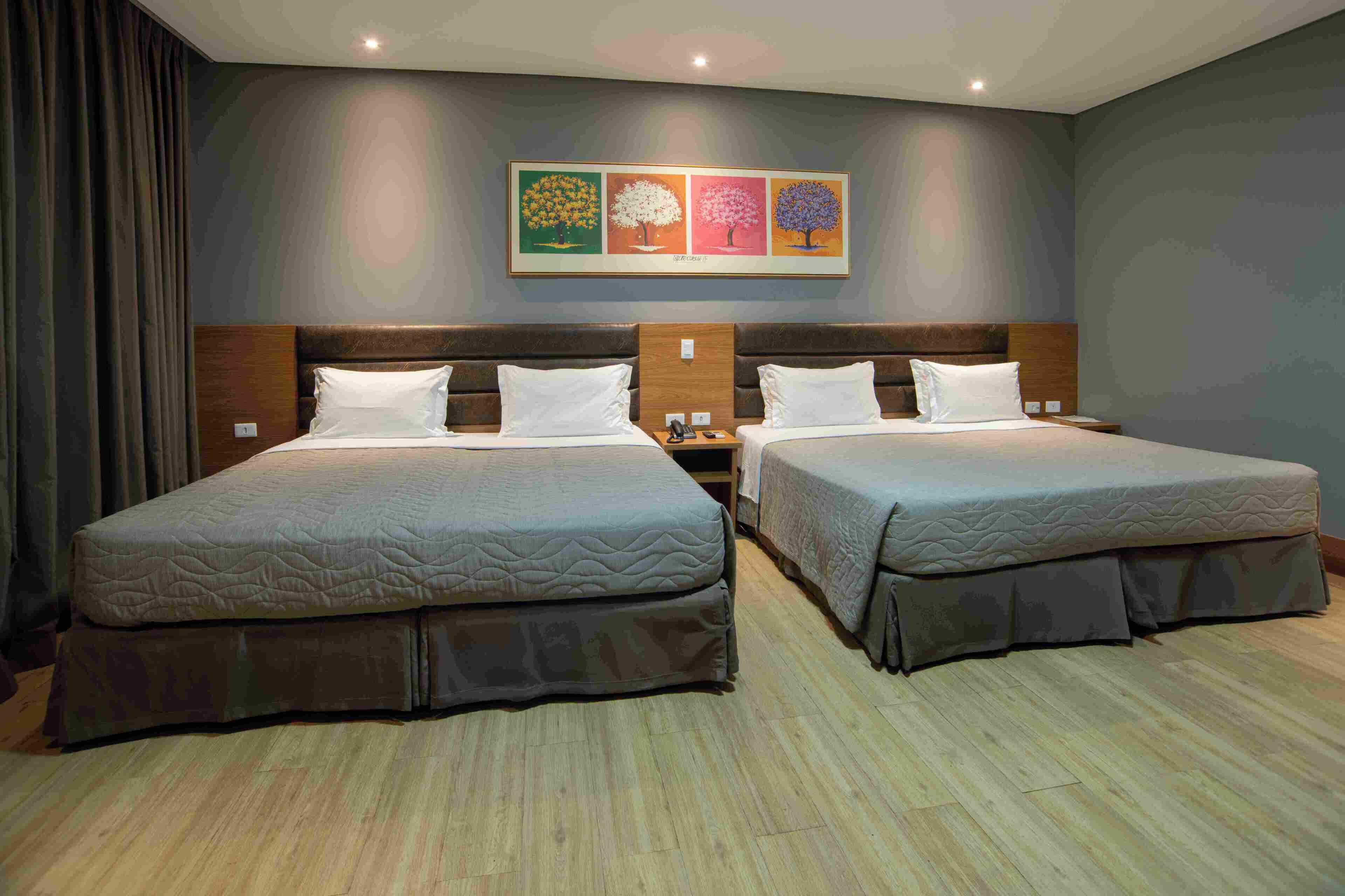 Habitación de hotel con dos camas, cabecera con un reloj y una obra de arte colgada en la pared.