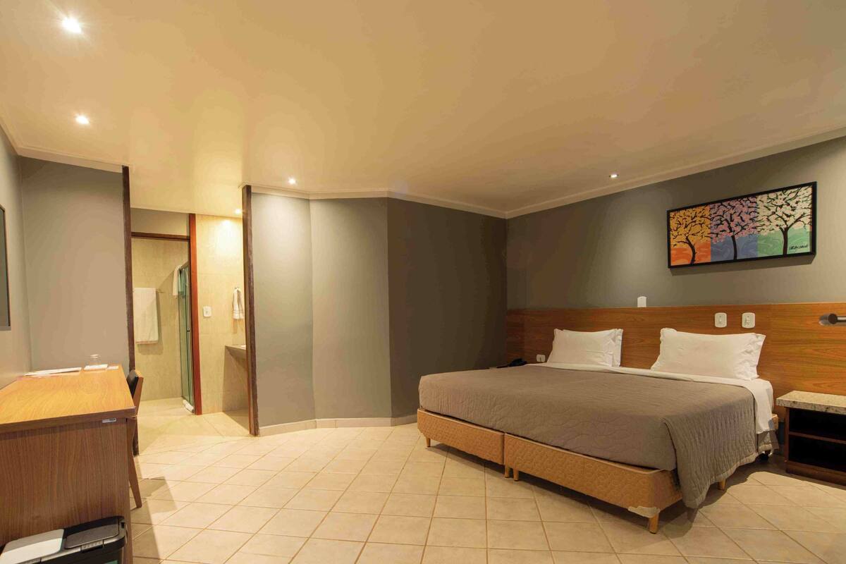 A modern hotel room with a bed, bedside table, and a painting on the wall.