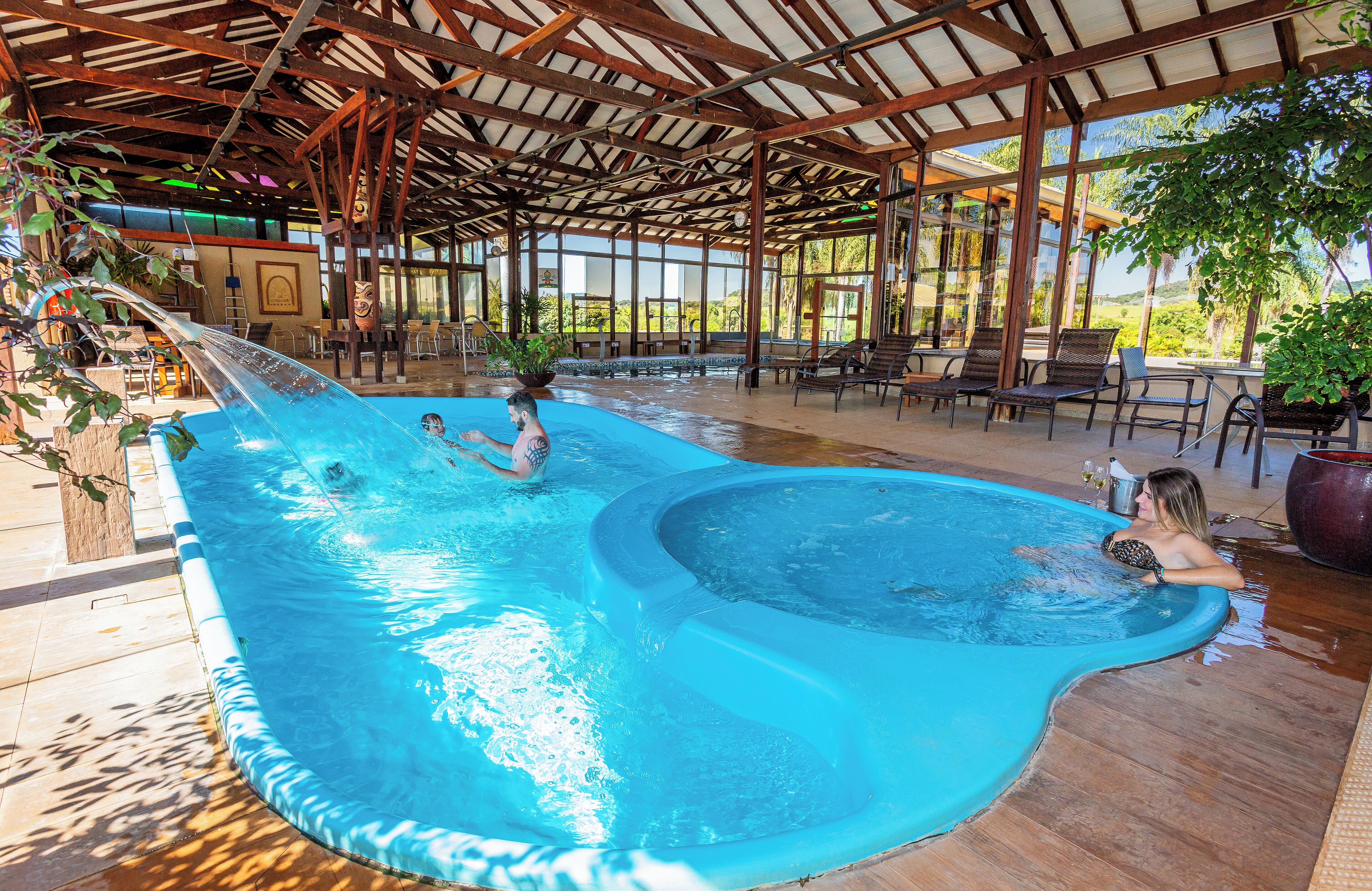 Uma piscina coberta com escorregador, espreguiçadeiras e plantas em vasos.