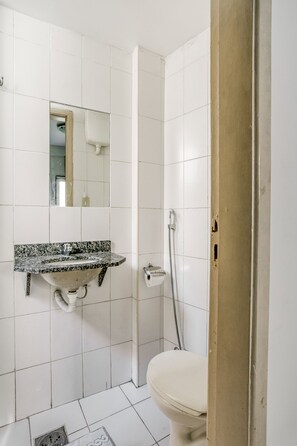Ein Badezimmer mit weiß gefliesten Wänden, einem Waschbecken mit Granitplatte, einer Toilette und einer Dusche mit Duschschlauch.