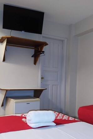 Ein Hotelzimmer mit einem Bett, einem an der Wand montierten Fernseher, einer Holzablage und einem kleinen Schreibtisch mit einem Computer.