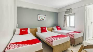 Quarto de hotel com três camas de solteiro, cada uma com um cobertor e travesseiro vermelhos, e um quadro na parede.