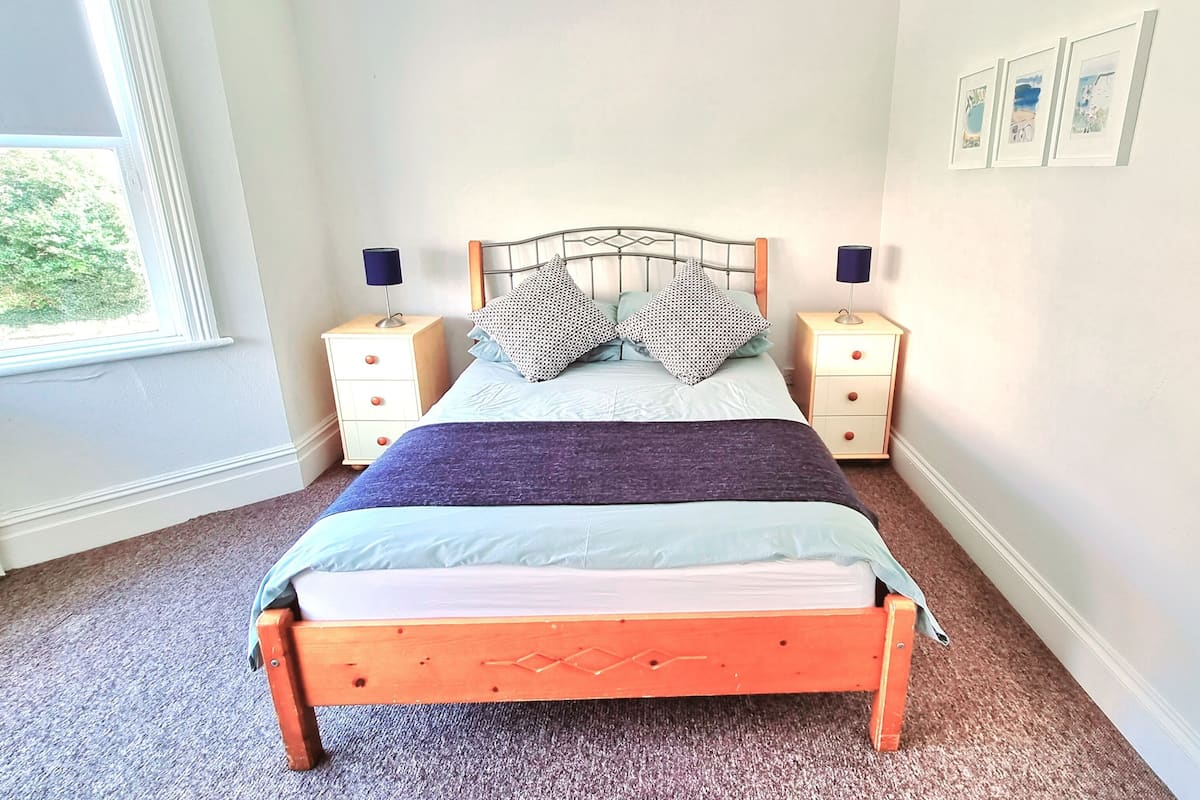 A bedroom with a bed, two nightstands, a window, and framed pictures on the wall.