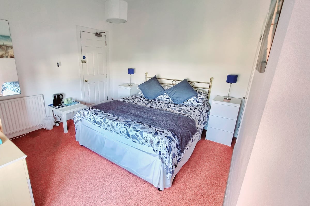 A bedroom with a bed, bedside tables, a desk, a chair, a radiator, and a mirror.