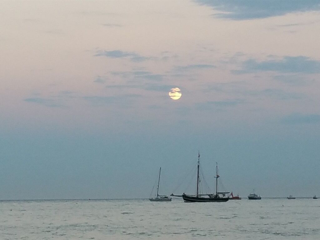 Mar calma com vários barcos, incluindo um veleiro e um barco a motor, sob um céu nublado.