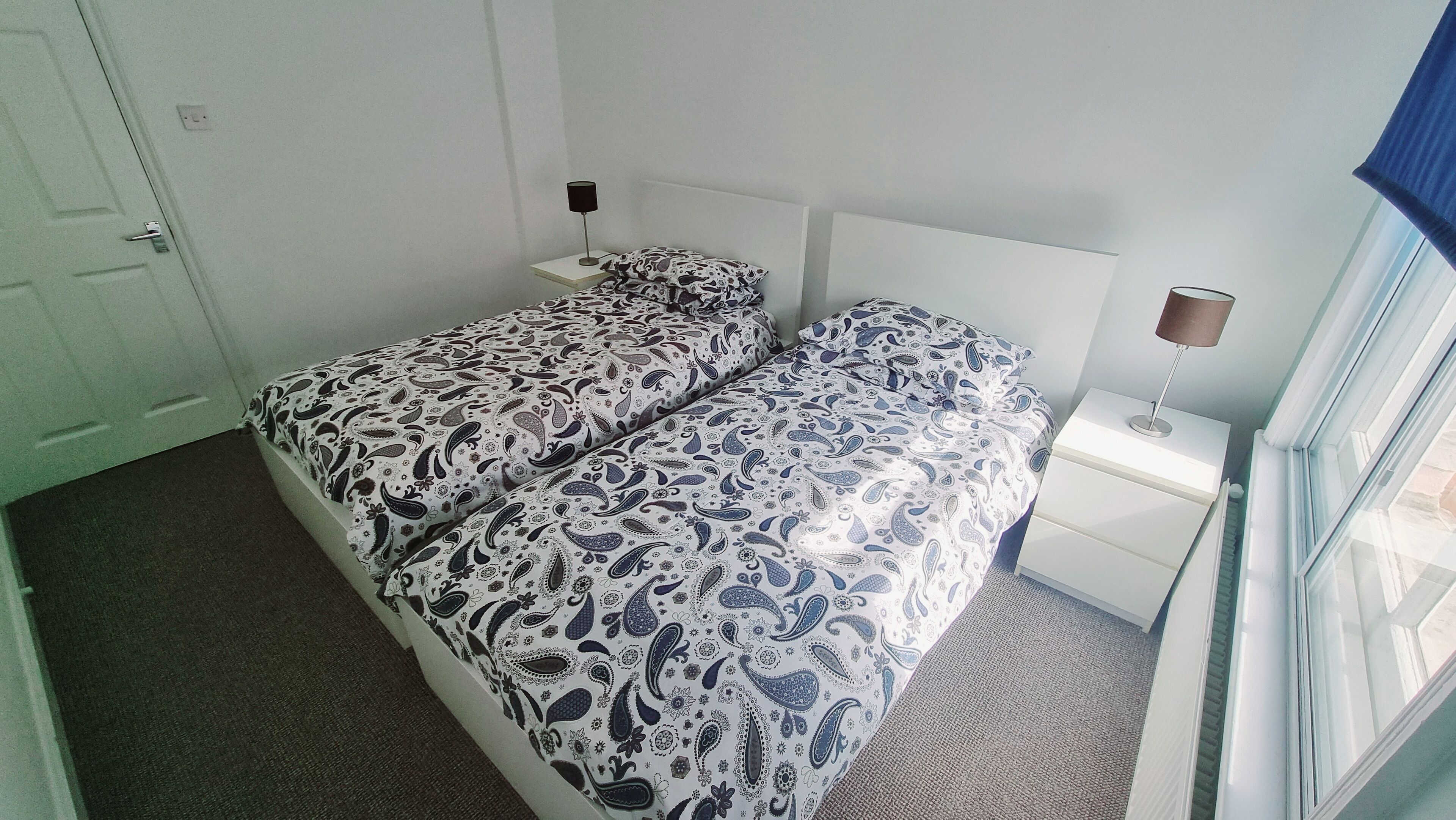A bedroom with two beds, a nightstand, a lamp, and a window with curtains.