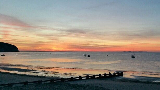 A beach with a wooden fence in the foreground and a sunset in the background.