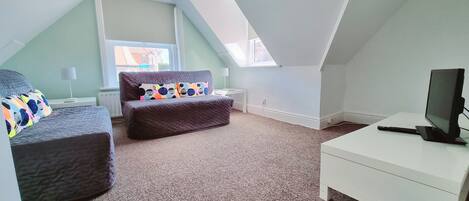 A cozy loft bedroom with a bed, a sofa, a desk, and a TV.