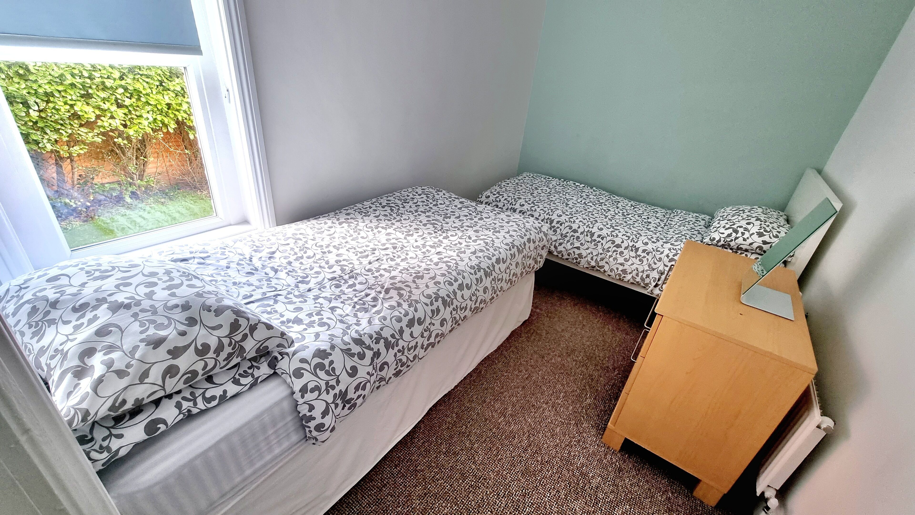 A small, single-room accommodation with two single beds, a wooden desk, and a radiator.