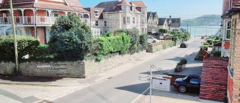 A street view with a row of traditional houses, a stone wall, and a clear view of the sea in the background.