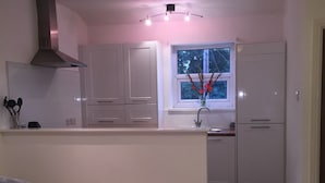 Cozinha moderna com armários brancos, janela com vista e sofá cinza na sala de estar.