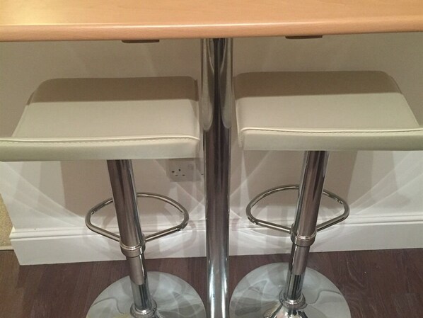 A bar stool with a chrome base and a white seat.