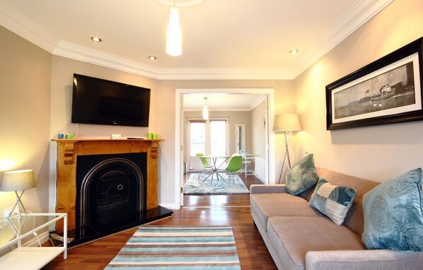 Una sala de estar con chimenea, sofá, televisión y un comedor al fondo.