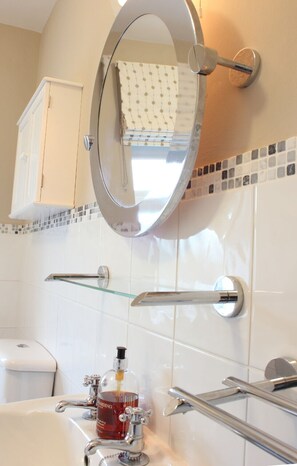 Bathroom features a round mirror, glass shelf, and a white toilet.