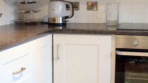 Une cuisine avec des armoires blanches, un four en acier inoxydable et une machine à café posée sur le plan de travail.