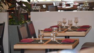 A restaurant with wooden tables and chairs, each set with wine glasses and red napkins.