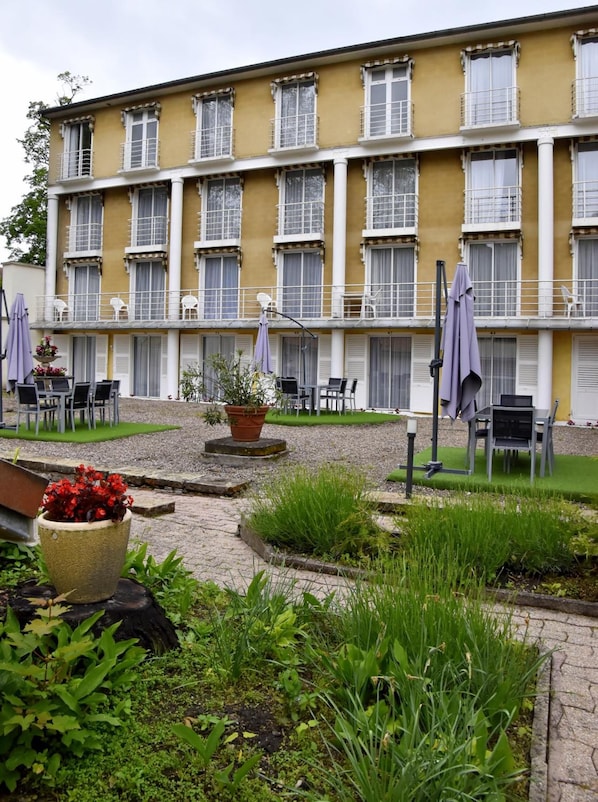 Un edificio amarillo con varios balcones, terraza al aire libre y un jardín con plantas en macetas.