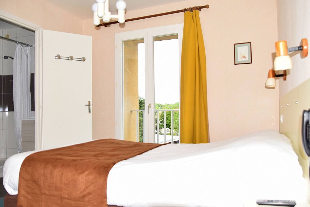 Habitación de hotel con cama, teléfono y vista al exterior.