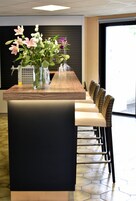 Un área de recepción con un mostrador de madera, un jarrón de flores y una zona de estar con sillas de mimbre.