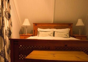 A bed with a wooden headboard, two bedside lamps, and a wooden bench at the foot of the bed. - Sweetie Pie Clarens Self Catering Cottages (Clarens)