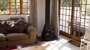 A cozy living room with a sofa, a fireplace, and large windows with curtains. - Sweetie Pie Clarens Self Catering Cottages (Clarens)