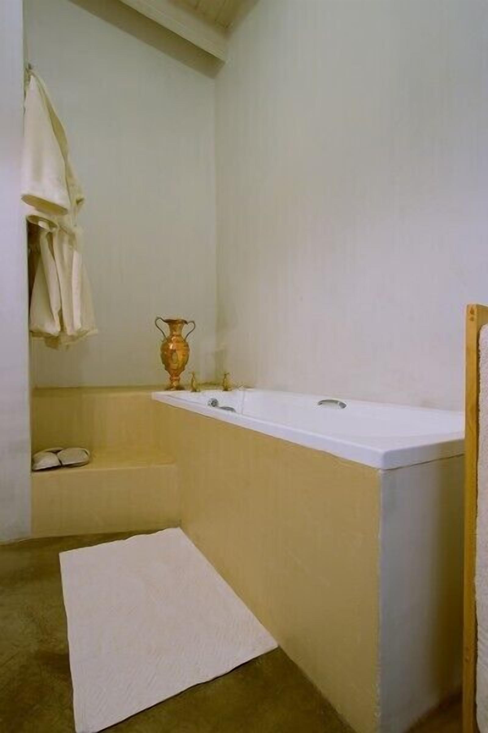 A bathroom with a bathtub, a sink, and a mirror. There is a towel rack with towels and a small shelf with a vase.