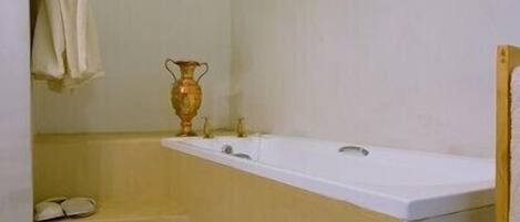 A bathroom with a bathtub, a sink, and a mirror. There is a towel rack with towels and a small shelf with a vase.