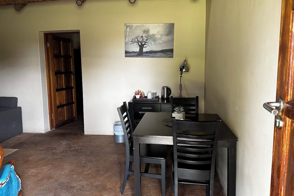 A dining area with a table, chairs, a lamp, and a painting on the wall.
