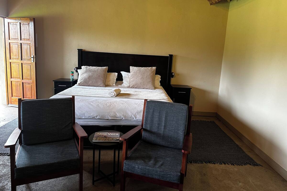 A bedroom with a bed, two chairs, a nightstand, and a wooden door.