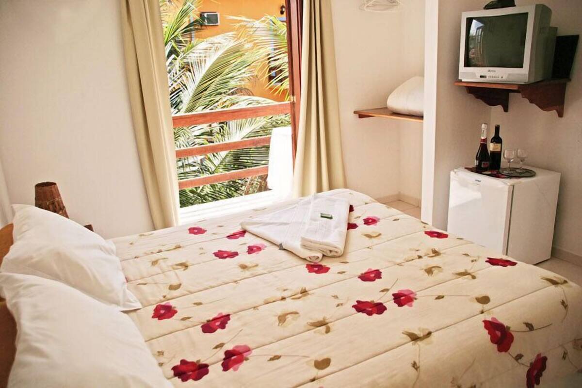 A hotel room with a bed, a television on a shelf, and a small refrigerator.