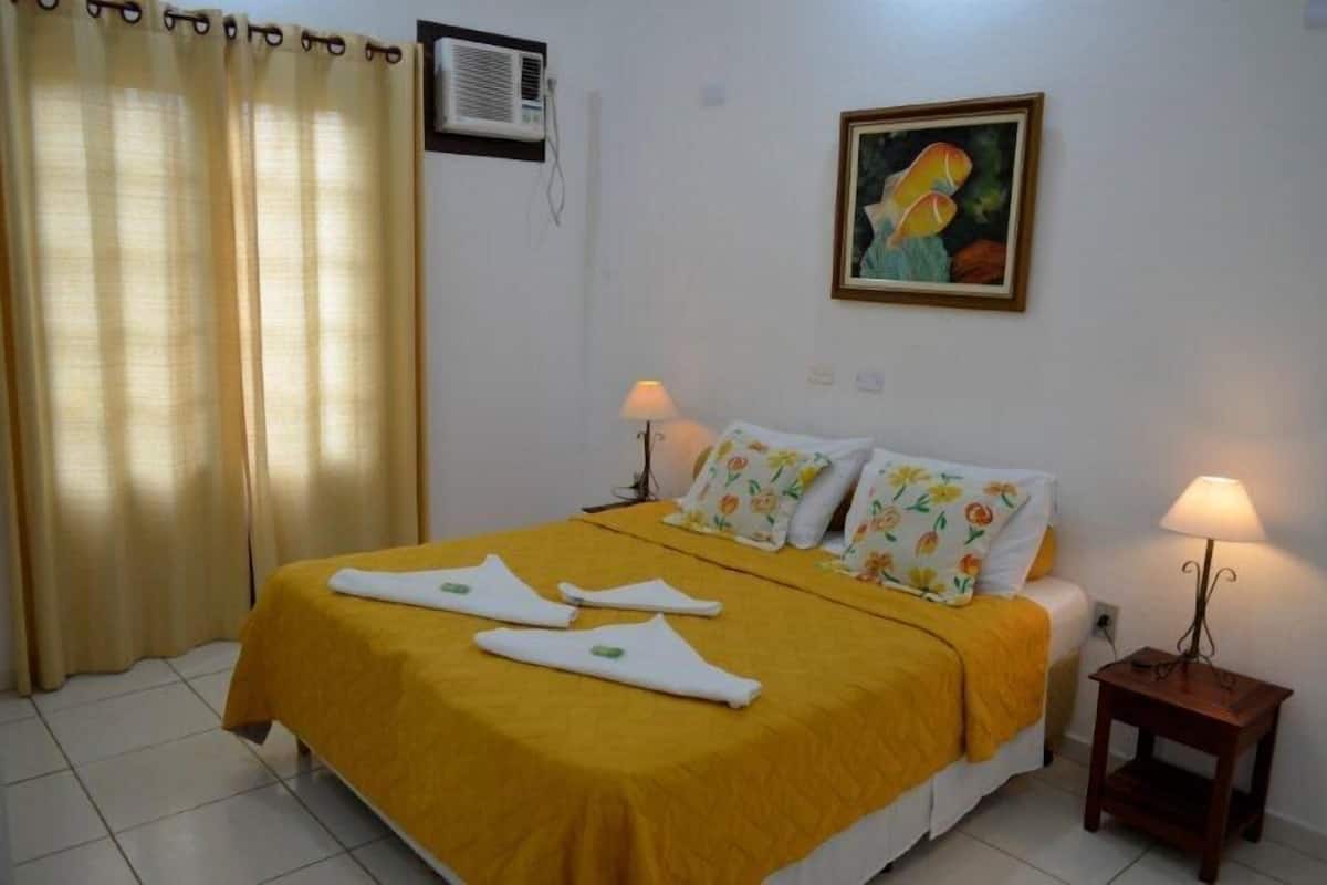 A hotel room with a bed, two bedside lamps, a painting on the wall, and a window with curtains.