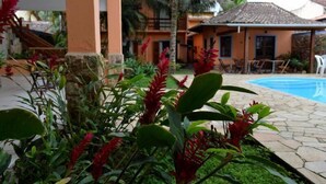 A poolside area with a stone patio, palm trees, and a building with a tiled roof. - Pousada Conchas de Paraty (Paraty)