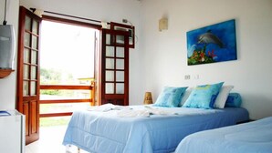 A bedroom with a bed, a painting of a dolphin, and a window with a view of greenery. - Pousada Conchas de Paraty (Paraty)
