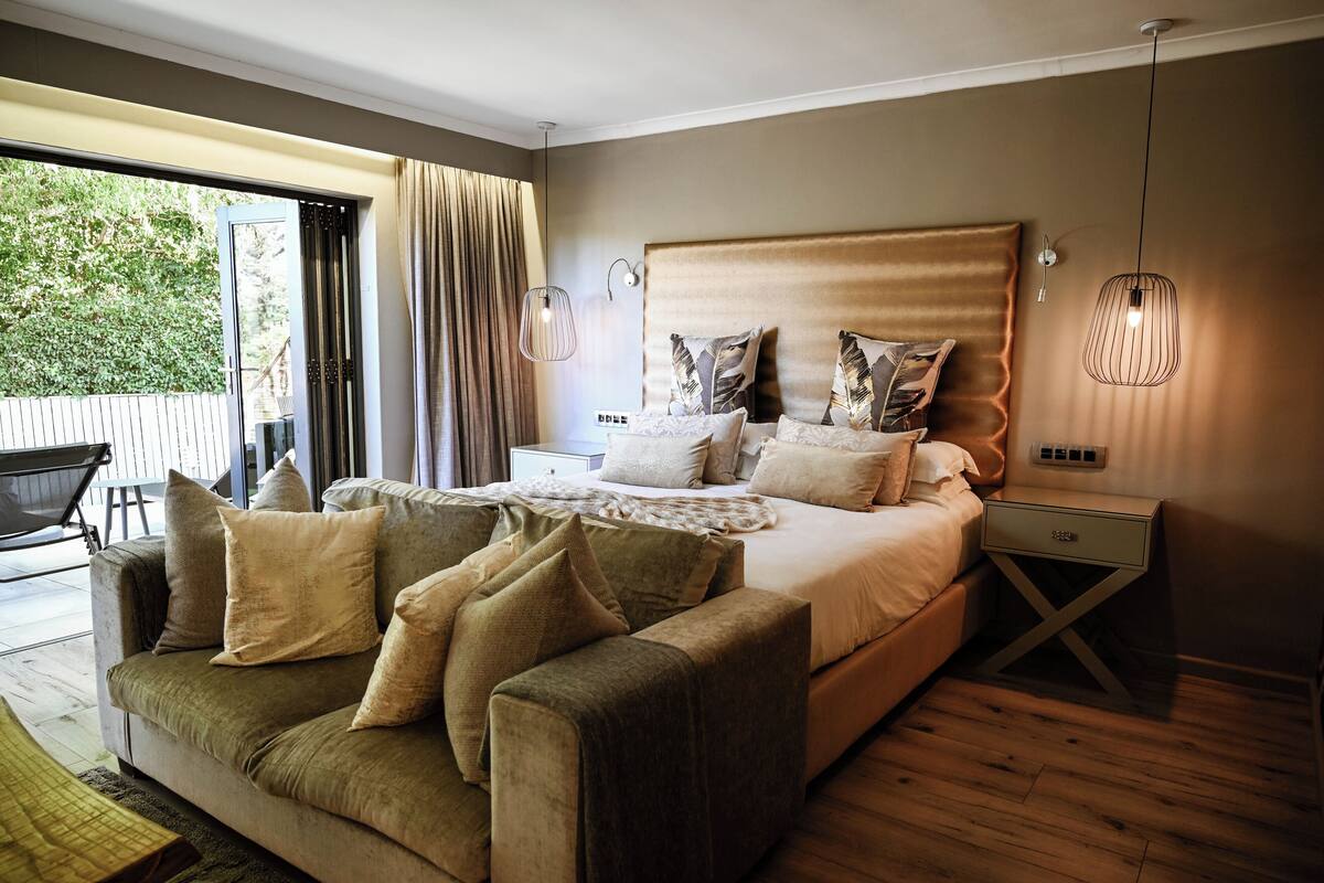 Un dormitorio con una cama grande, un sofá, una mesita de noche y vistas al exterior.