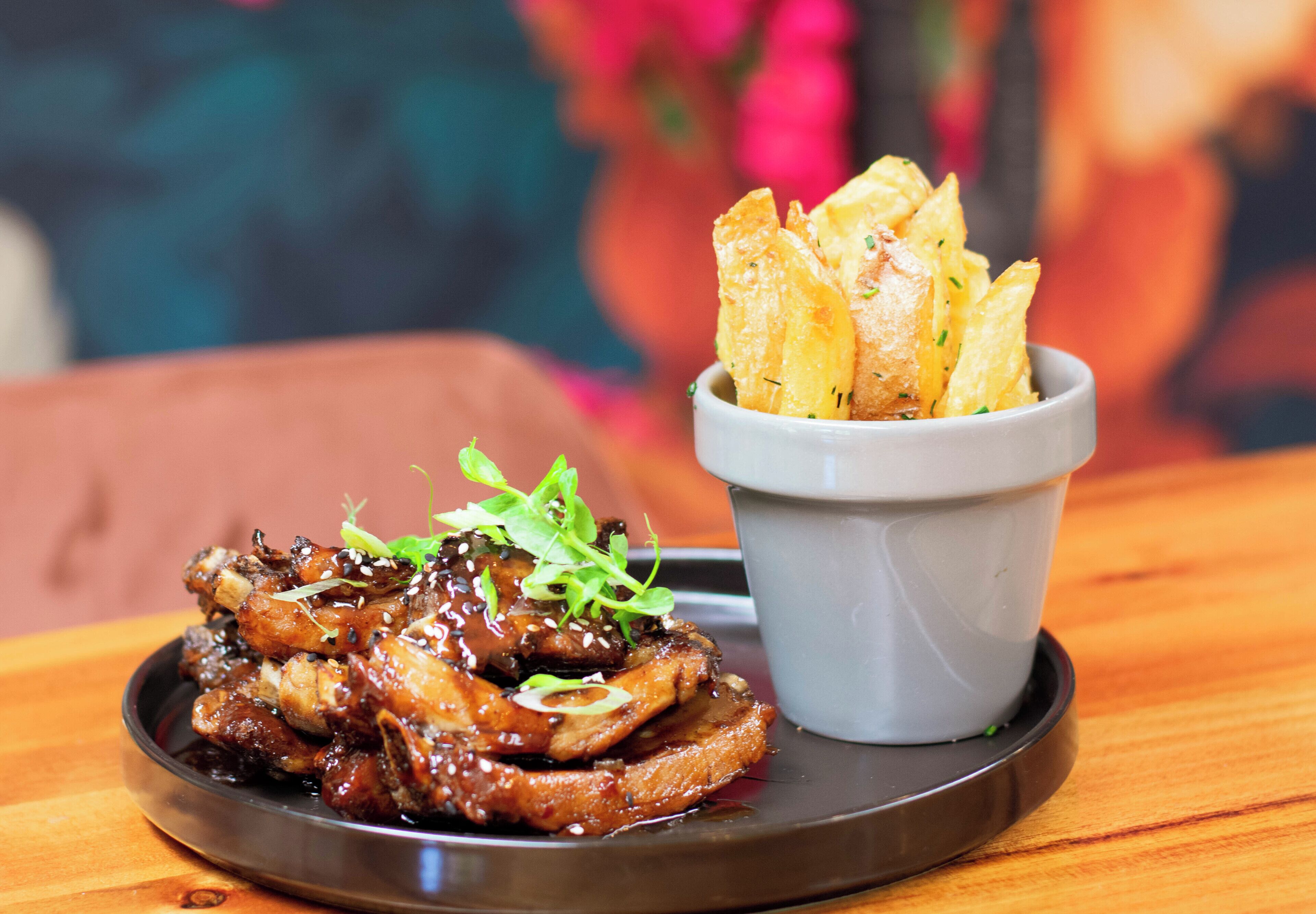 A plate of glazed meat with a side of crispy potato chips on a wooden table.