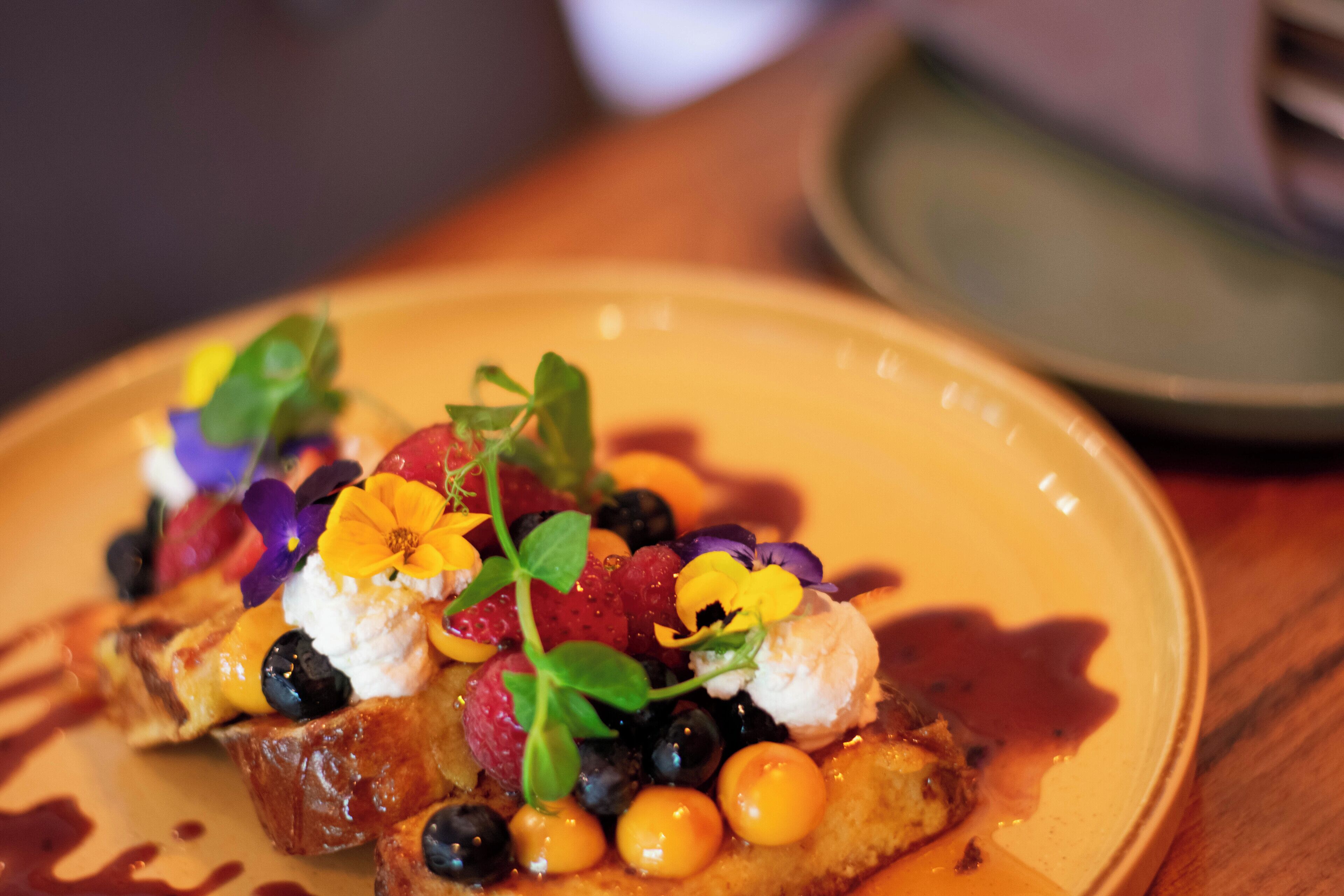 Un plato con un postre cubierto de frutos rojos, crema y flores.