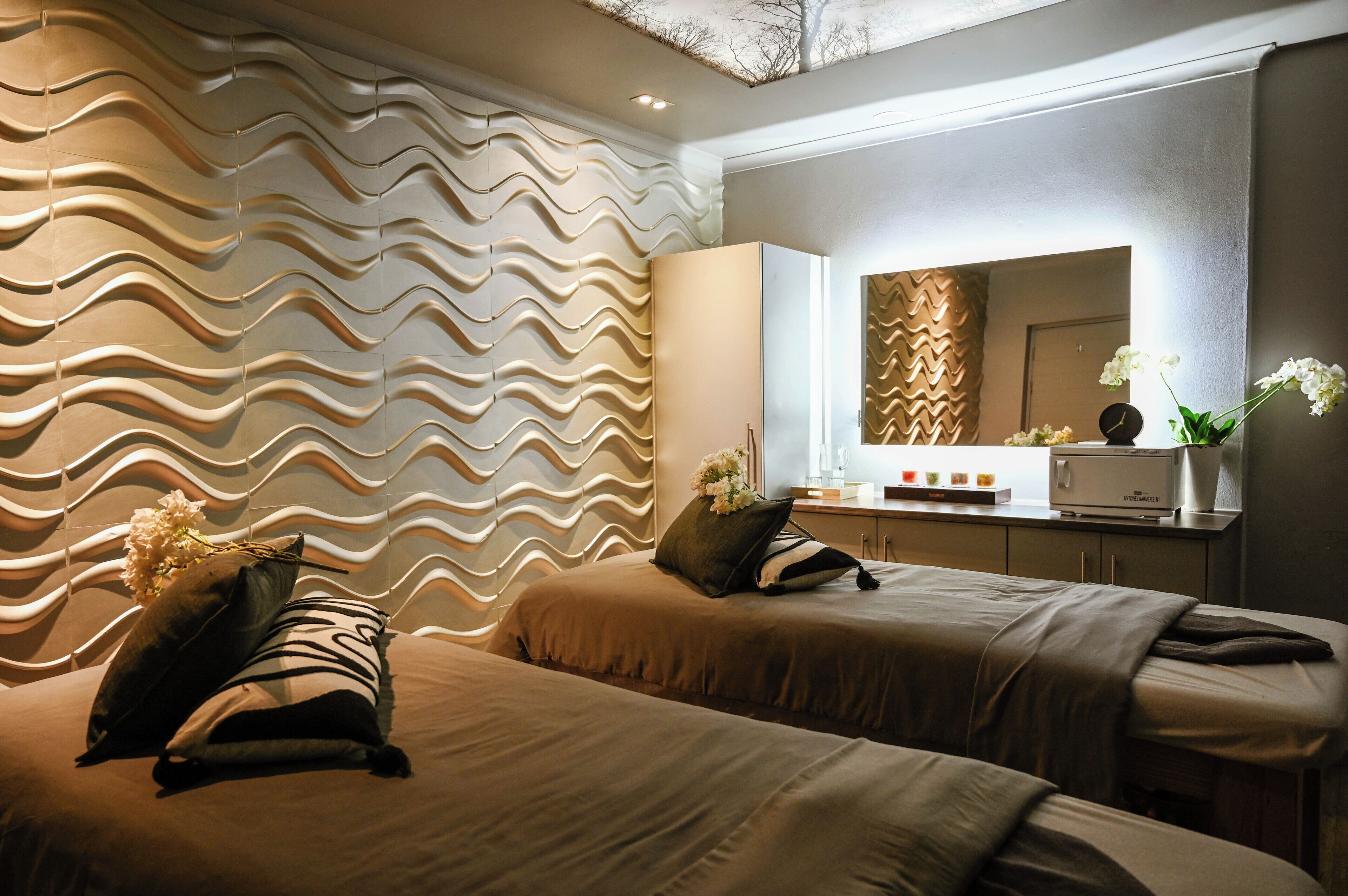 A modern hotel room with two beds, a large mirror, and a wall with a wavy pattern.