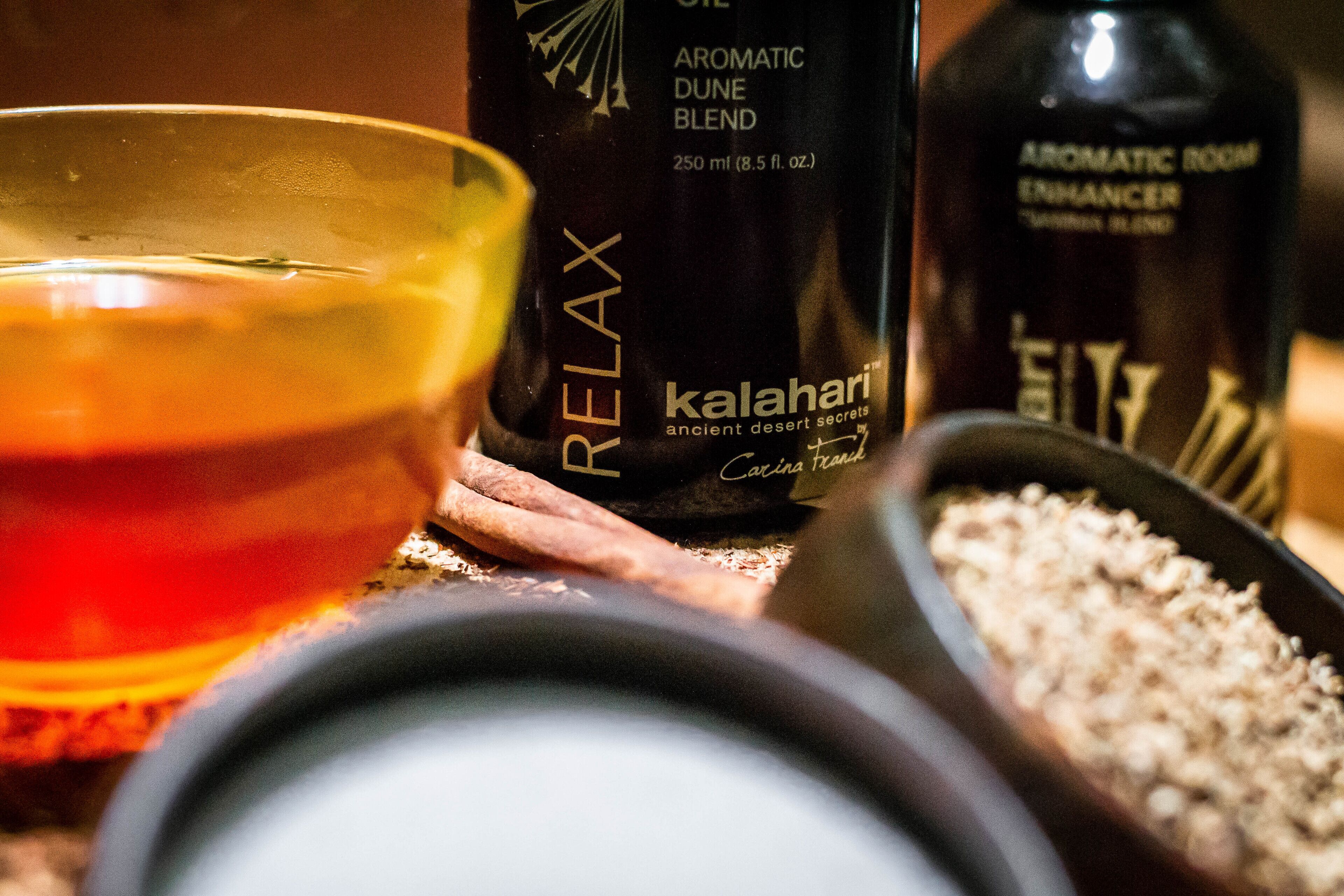 A bottle of Relax aromatherapy oil, a bowl of oil, and a container of essential oils on a wooden surface.